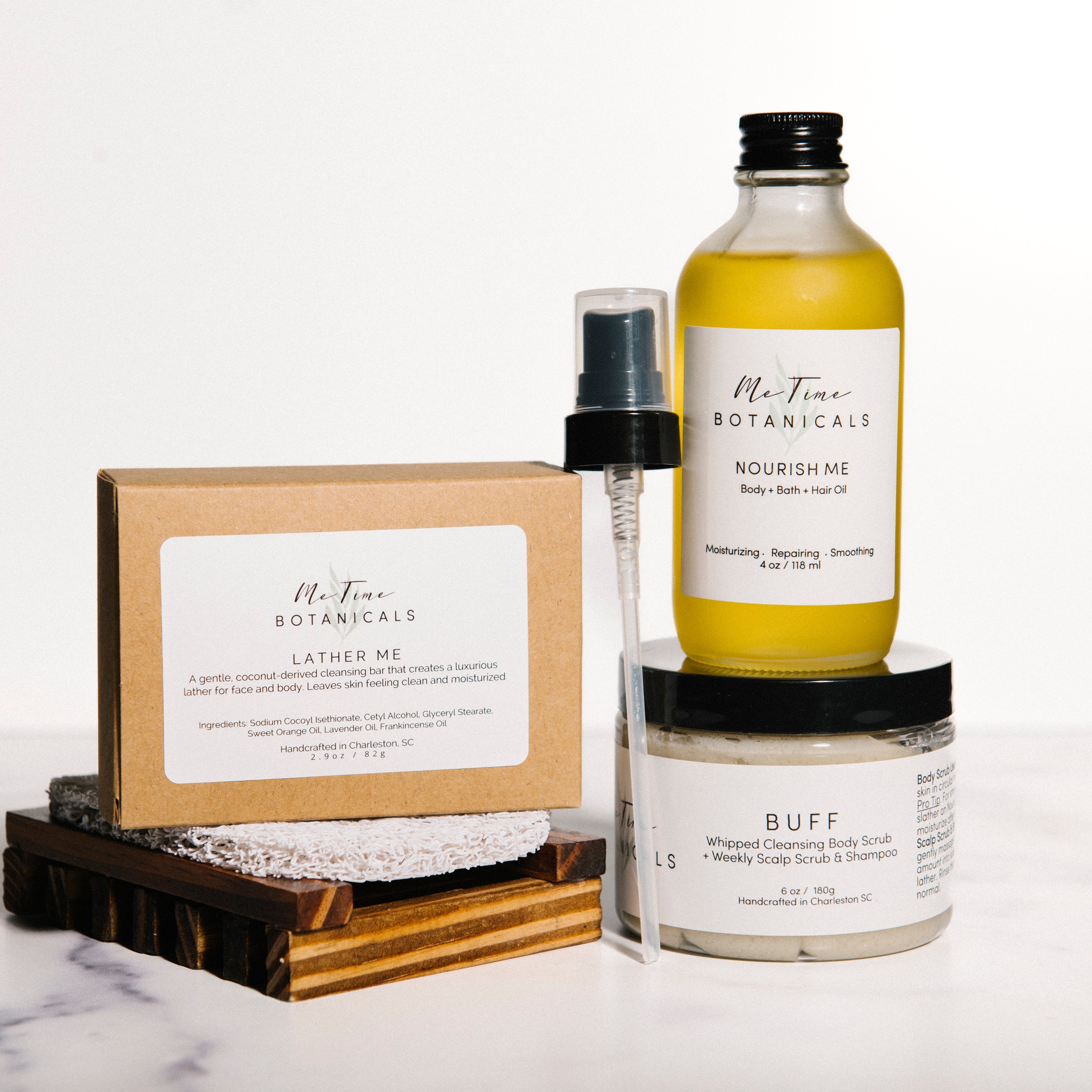 A Me Time Botanicals bath and body set arranged on a white marble surface against a white background.
